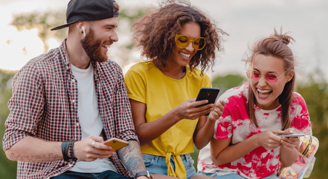 imagem pessoas sorrindo segurando celular Pague menos nas suas compras com os principais cupons disponíveis hoje